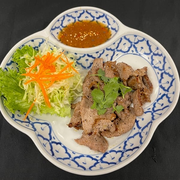 Grilled beef slices with cilantro, shredded cabbage, carrots, and a spicy dipping sauce on a patterned plate.