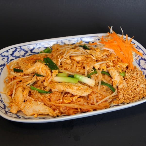 Chicken Pad Thai with bean sprouts, green onions, shredded carrots, and crushed peanuts on a white plate.