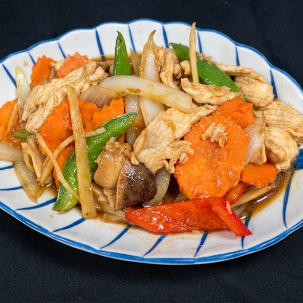 Stir-fried chicken with carrots, onions, mushrooms, and green beans on a white and blue plate.