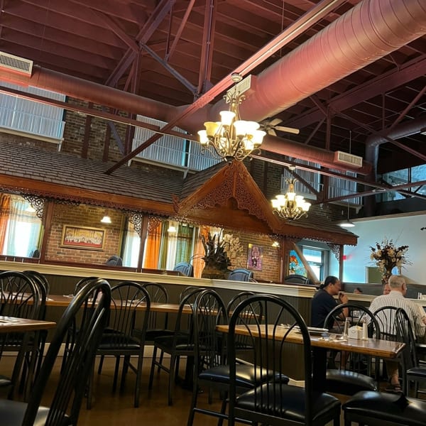 Restaurant interior with exposed brick, red ceiling, ornate wooden decor, and diners at tables.