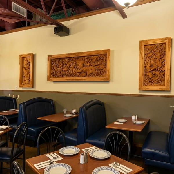Restaurant interior with blue booths, wooden tables set with plates, and ornate carved wooden wall art.